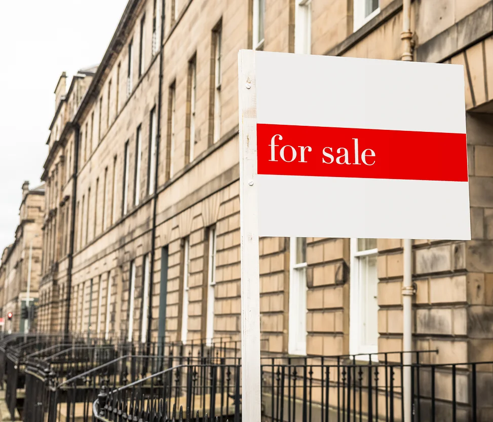 For sale sign outside a row of traditional stone terraced houses.