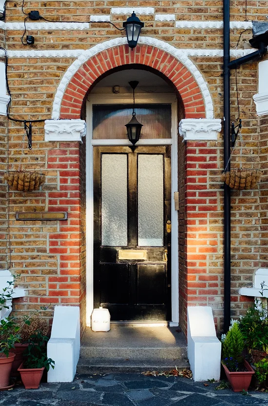 Black front door of a traditional brick house with red and white arch detailing.